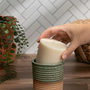 Refillable soy candle being placed into a handmade green and tan ceramic jar. Sustainable and phthalate-free home decor.