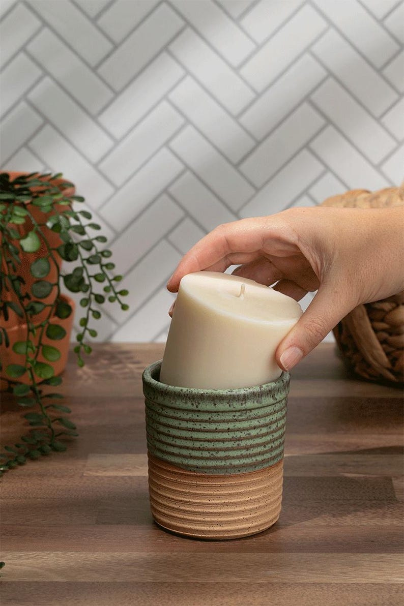 Refillable soy candle being placed into a handmade green and tan ceramic jar. Sustainable and phthalate-free home decor.