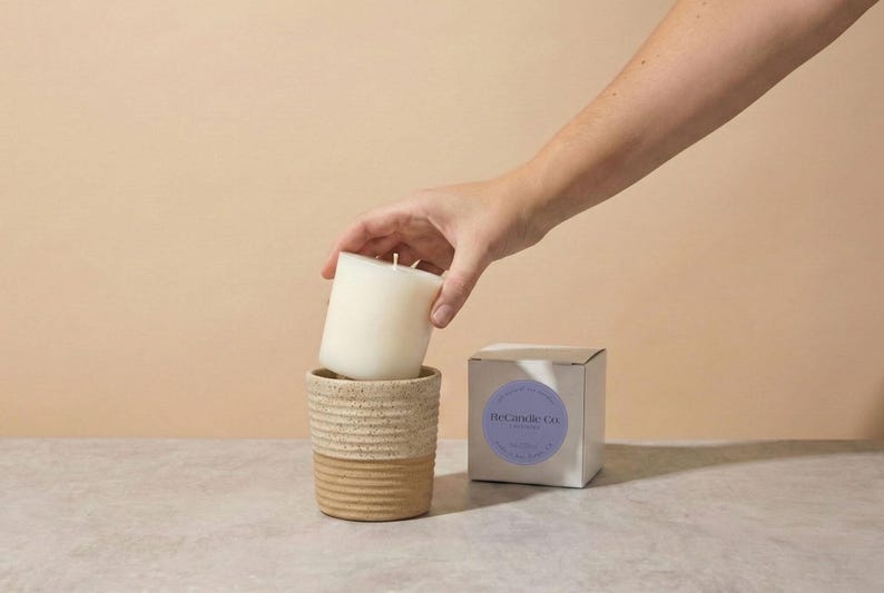 A lavender scented soy wax candle refill being placed into a handmade, ceramic refillable candle jar