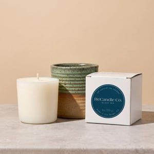 A Black Sea scented soy wax candle refill placed next to it’s box and a handmade, ceramic refillable candle jar