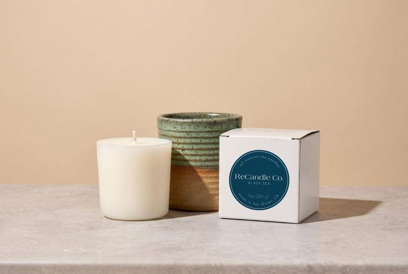 A Black Sea scented soy wax candle refill placed next to it’s box and a handmade, ceramic refillable candle jar
