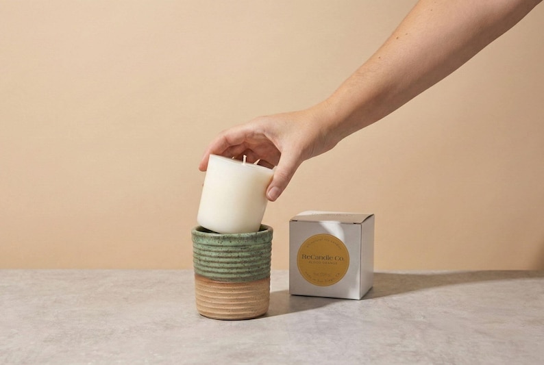 A blood orange scented soy wax candle refill being placed into a handmade, ceramic refillable candle jar