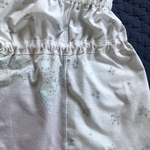 Pu&ograve; includere: Tessuto bianco con un motivo floreale con piccoli fiori viola e blu. Il tessuto &egrave; arricciato nella parte superiore e inferiore con un bordo a balze. Il design include spalline e una cucitura al centro.