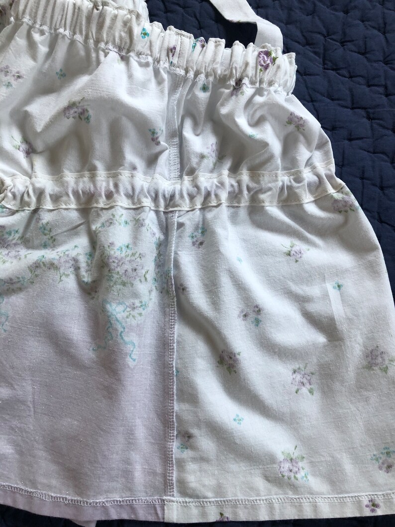 Pu&ograve; includere: Tessuto bianco con un motivo floreale con piccoli fiori viola e blu. Il tessuto &egrave; arricciato nella parte superiore e inferiore con un bordo a balze. Il design include spalline e una cucitura al centro.