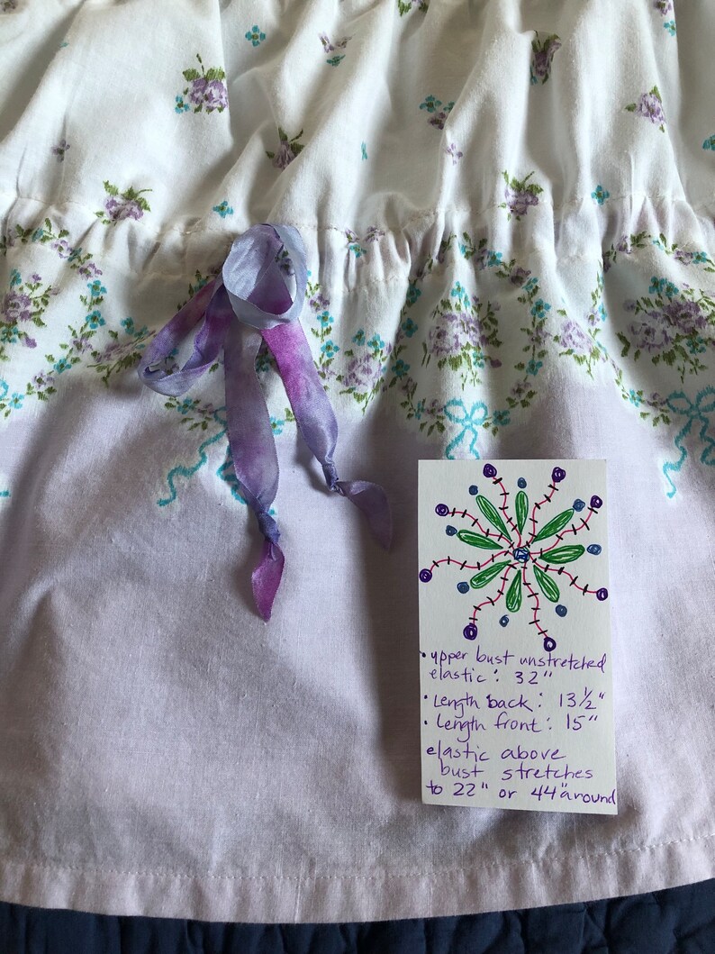 Pu&ograve; includere: Abito in tessuto bianco con motivo floreale viola e turchese. L'abito ha uno scollo a balze e un fiocco di nastro viola. L'etichetta recita: busto superiore non allungato: 81 cm, lunghezza schiena: 34 cm, lunghezza davanti: 38 cm.