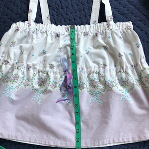 Pu&ograve; includere: Un top con stampa floreale bianca e lavanda con spalline regolabili. Il top presenta una vita arricciata e un nastro decorativo. La lunghezza del top &egrave; di circa 40 cm.