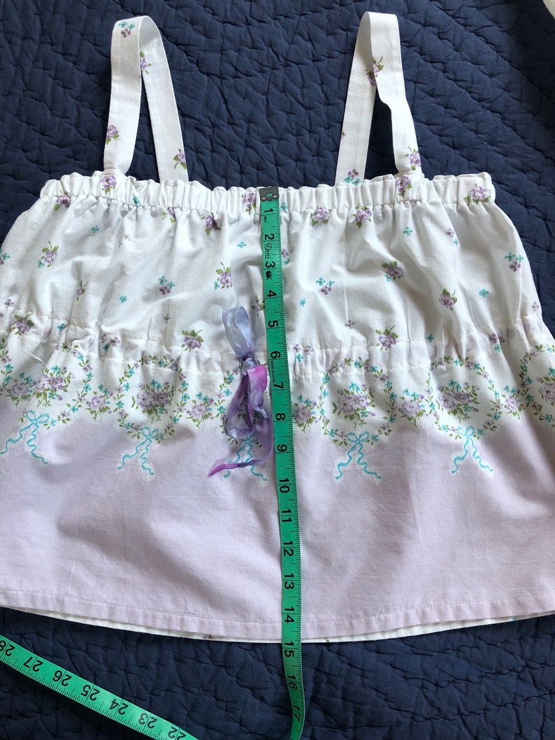 Pu&ograve; includere: Un top con stampa floreale bianca e lavanda con spalline regolabili. Il top presenta una vita arricciata e un nastro decorativo. La lunghezza del top &egrave; di circa 40 cm.