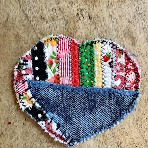 May include: A heart-shaped fabric patch constructed from various textile scraps, including a dark blue denim section at the bottom and vertical strips of floral, polka dot, striped, and solid colored cotton fabrics joined with visible black zigzag stitching.