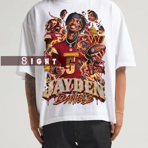 May include: A white short-sleeve t-shirt featuring a graphic print of football player Jayden Daniels in a burgundy and gold Commanders jersey. The design includes the text "JAYDEN DANIELS," "8IGHT," "COMMANDERS," and "HAIL," along with football imagery.