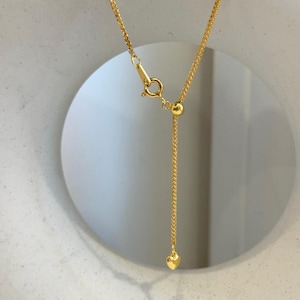 May include: A gold-colored necklace with a delicate chain and a small heart pendant. The necklace features an adjustable design with a sliding bead and a clasp closure. The heart pendant is approximately 0.25 inches in size.