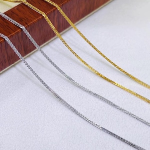 May include: Two thin wheat chain necklaces, one in a polished silver tone and one in a polished gold tone. The chains feature a braided, interlocking link design that creates a smooth, continuous texture along the length of each individual strand.