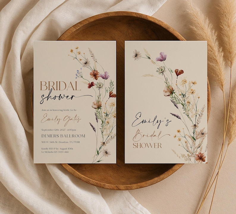 A minimalist bridal shower invitation template with a light beige background. On the right side, there is a delicate watercolor arrangement of wildflowers and dried grasses in earthy tones of rust, purple, and cream. The typography is a mix of modern serif and elegant script fonts.