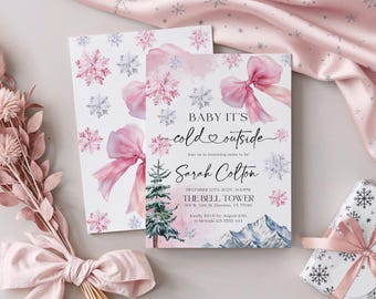 Puede incluir: Invitaciones para baby shower con temática invernal. Las tarjetas presentan lazos rosas, copos de nieve y el texto "Baby it's cold outside". También se ve un regalo envuelto en papel de copos de nieve y cinta rosa.