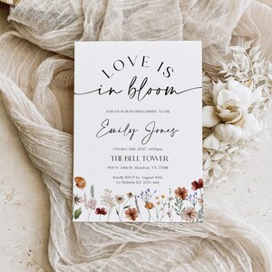 Minimalist bridal shower invitation with “Love is in Bloom” script, soft white background, and a border of colorful wildflowers in rustic tones.