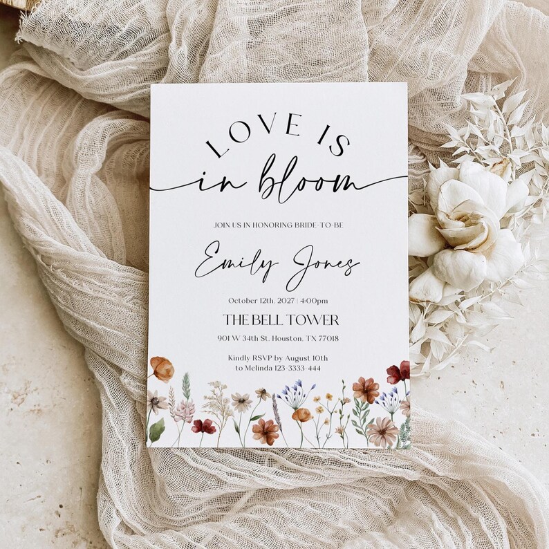 Minimalist bridal shower invitation with “Love is in Bloom” script, soft white background, and a border of colorful wildflowers in rustic tones.