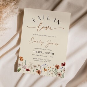Fall in Love" bridal shower invitation with modern calligraphy, autumn wildflowers border, and minimalist neutral background.