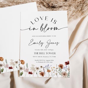 Minimalist bridal shower invitation with “Love is in Bloom” script, soft white background, and a border of colorful wildflowers in rustic tones.
