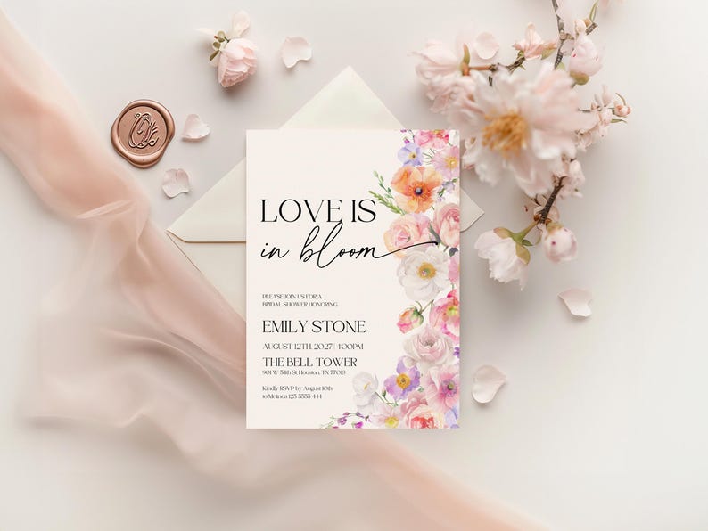 May include: A white card with a floral design border. The text "LOVE IS in bloom" is in black script font. The card is an invitation to a bridal shower for Emily Stone on August 12th, 2027 at 4:00 PM at The Bell Tower.