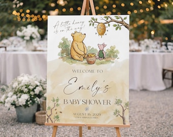 Op de afbeelding: Een welkomstbord voor een babyshower met illustraties van Winnie de Poeh en Knorretje. Het bord luidt "A little honey is on the way!" en verwelkomt gasten op de babyshower van Emily op 16 augustus 2029 in Coral Springs, Florida.