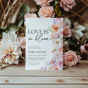 May include: A white wedding shower invitation with a floral design. The text reads "Love is in bloom" and includes the bride's name, Emily Stone, the date and time of the shower, and the location, The Bell Tower.