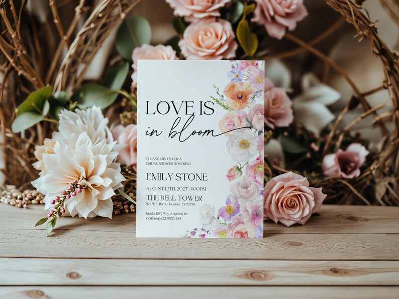 May include: A white wedding shower invitation with a floral design. The text reads "Love is in bloom" and includes the bride's name, Emily Stone, the date and time of the shower, and the location, The Bell Tower.