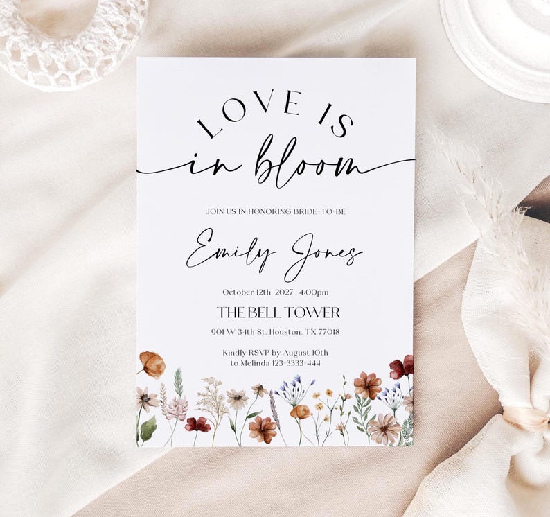 May include: A white invitation card with the text "LOVE IS in bloom" in elegant script. The card includes details for a wedding, with the bride's name, date, time, and location, and a floral border at the bottom.