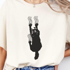 Climbing Cat T-Shirt, playful black cat silhouette with scratch marks, minimalist funny pet design for feline fans, crew neck unisex shirt