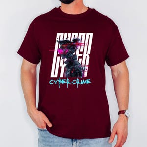 Può includere: Una maglietta bordeaux con un design grafico futuristico. Il design include il testo "CYBER UTTER" in lettere bianche e "CYBER CRIME" in una sceneggiatura turchese. La grafica raffigura un cyborg con accenti rosa e neri.