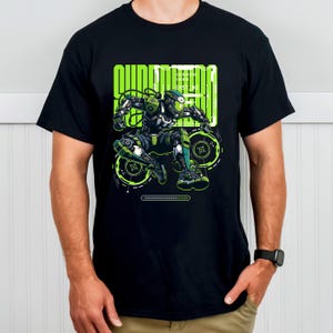 Peut inclure: T-shirt noir avec un motif de robot futuriste vert et gris. Le robot est en mouvement, avec le mot "QUANTUM" en vert néon au-dessus. Le design comprend des détails techniques. Col rond classique.