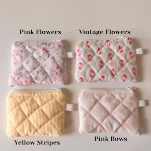 May include: Four quilted zipper pouches with different patterns. The pouches are pink with pink flowers, pink with vintage flowers, yellow with yellow stripes, and pink with pink bows. The pouches are all the same size and shape.