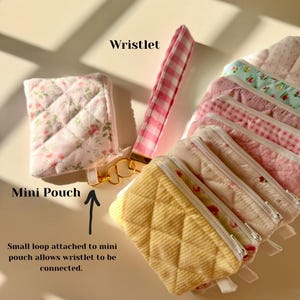 May include: A set of small quilted fabric pouches with floral and gingham patterns. The pouches have a zipper closure and a small loop to attach a wristlet. The wristlet is pink and white gingham.