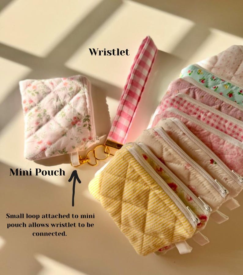 May include: A set of small quilted fabric pouches with floral and gingham patterns. The pouches have a zipper closure and a small loop to attach a wristlet. The wristlet is pink and white gingham.