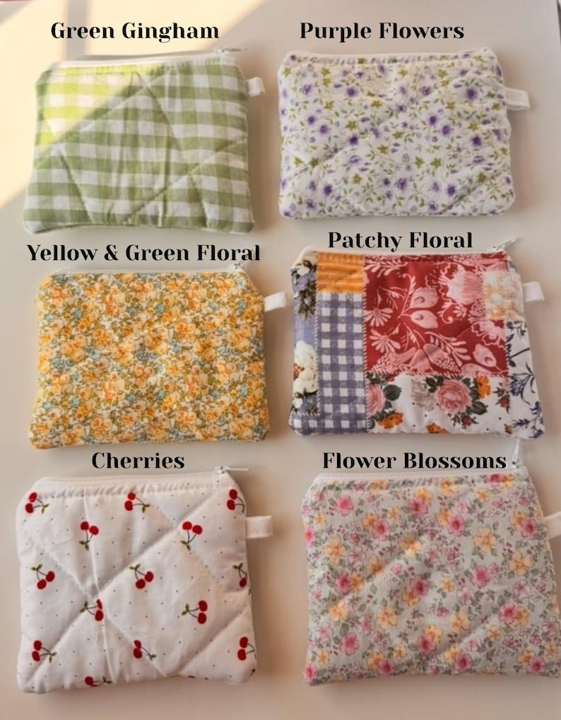 May include: Six small, quilted pouches with zippers, each featuring a unique fabric design. Patterns include green gingham, purple flowers, yellow and green floral, patchwork floral, cherries, and flower blossoms. The pouches are arranged on a white surface.