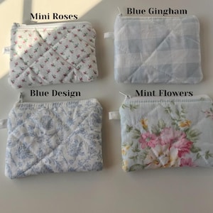 May include: Four small, quilted fabric pouches with zippers. The pouches feature different patterns: mini roses, blue gingham, blue design, and mint flowers. Each pouch has a small fabric loop attached to the zipper.
