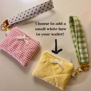 May include: Three small fabric wallets in pink gingham, yellow quilted, and white floral patterns, each with a white bow and a zipper. Matching wrist straps in coordinating patterns are also shown. Text reads: "Choose to add a small white bow to your wallet!"