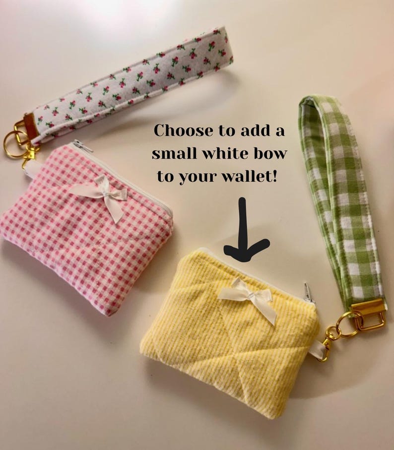 May include: Three small fabric wallets in pink gingham, yellow quilted, and white floral patterns, each with a white bow and a zipper. Matching wrist straps in coordinating patterns are also shown. Text reads: "Choose to add a small white bow to your wallet!"
