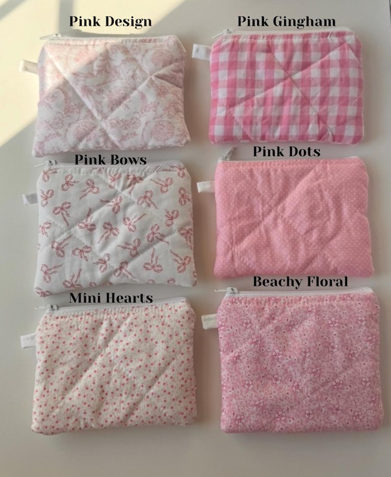 May include: A collection of small, quilted fabric pouches in various pink patterns. Designs include floral, gingham, polka dots, bows, and mini hearts. Each pouch has a zipper closure and a small fabric loop.