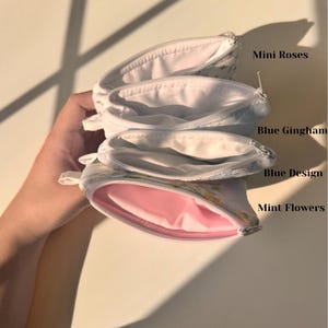 May include: Four small, open zippered pouches with floral patterns. The pouches are labeled "Mini Roses", "Blue Gingham", "Blue Design", and "Mint Flowers". The interior of the "Mint Flowers" pouch is pink.