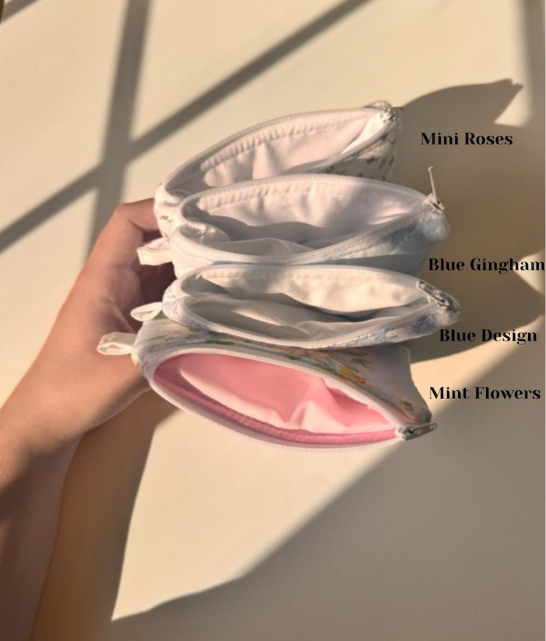 May include: Four small, open zippered pouches with floral patterns. The pouches are labeled "Mini Roses", "Blue Gingham", "Blue Design", and "Mint Flowers". The interior of the "Mint Flowers" pouch is pink.