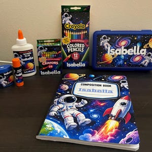 May include: A collection of school supplies featuring space-themed designs with astronauts, planets, and rockets. Items include a composition book, a blue pencil case, a box of 12 coloured pencils, a box of 24 crayons, a glue stick, and a bottle of school glue.