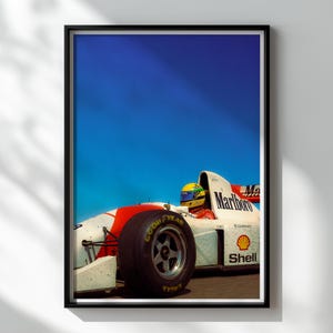 May include: Framed print featuring a vintage Formula 1 race car with a red and white design, the Marlboro logo, and a driver in a yellow helmet. The car has a Goodyear tire and a Shell logo against a bright blue sky.