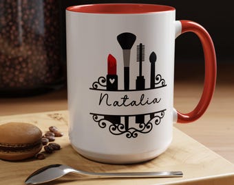 Può includere: Tazza in ceramica bianca con interno e manico rossi. La tazza presenta una grafica nera di strumenti per il trucco e il nome "Natalia" in un carattere decorativo. È incluso anche un rossetto rosso con un cuore.