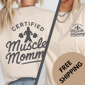Puede incluir: Una camiseta beige con el texto "CERTIFIED Muscle Mommy" y una silueta de una mujer levantando pesas en la espalda. La parte delantera de la camiseta tiene el texto "CERTIFIED Muscle Mommy" en una fuente más pequeña. La camiseta está en una modelo y tiene un círculo marrón con el texto "FREE SHIPPING" en el lado derecho de la imagen.