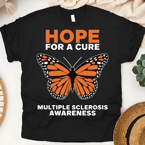 Könnte beinhalten: Schwarzes T-Shirt mit einem weißen Schmetterlings-Motiv und dem Text "HOPE FOR A CURE" und "MULTIPLE SCLEROSIS AWARENESS".