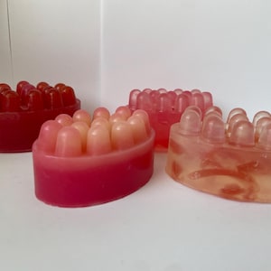 May include: Three oval-shaped bath soaps with raised bumps. The soaps are in shades of pink and clear.
