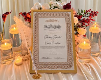 May include: A gold-framed marriage certificate featuring black text and intricate brown borders, displayed with a white feather quill pen, surrounded by four glass candle holders with lit candles and a floral arrangement of white and red roses.
