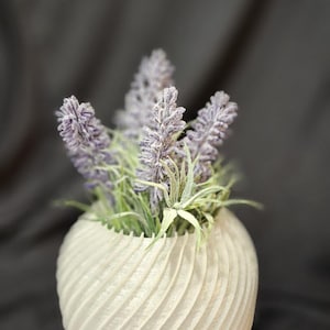 May include: A white ceramic planter with a swirling, textured design. The planter is filled with a small arrangement of purple lavender flowers.