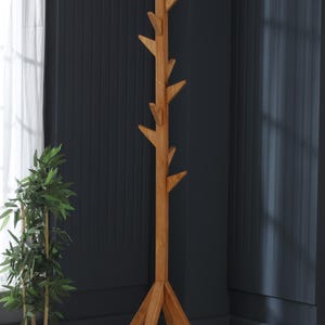Può includere: Un appendiabiti in legno con un design a forma di ramo d'albero. L'appendiabiti ha una base triangolare e diversi rami per appendere cappotti, cappelli o sciarpe.