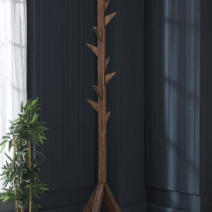Puede incluir: Un perchero de madera marrón con un diseño de rama de árbol y una base triangular. El perchero tiene varios ganchos para colgar abrigos, sombreros o bufandas.