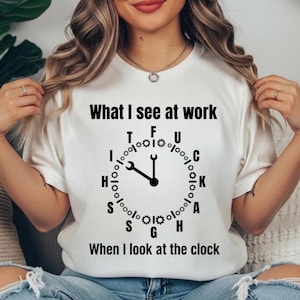 May include: White t-shirt with the text "What I see at work" above a clock design made of tools and gears. The clock hands point to 12 o'clock. Below the clock is the text "When I look at the clock."